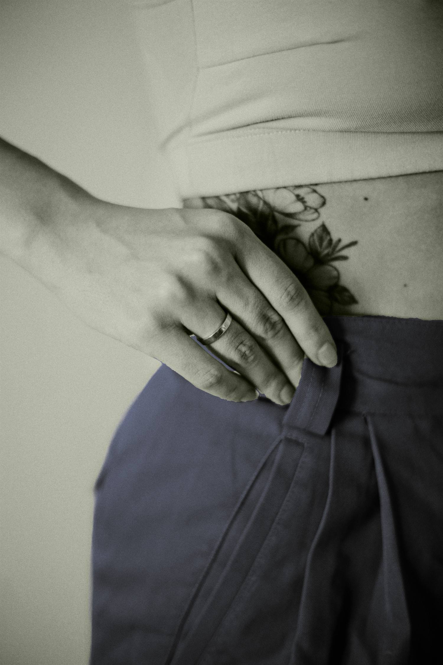 Close detail of a hand at the trouser waistband, showing the pleat and the flat-lying band