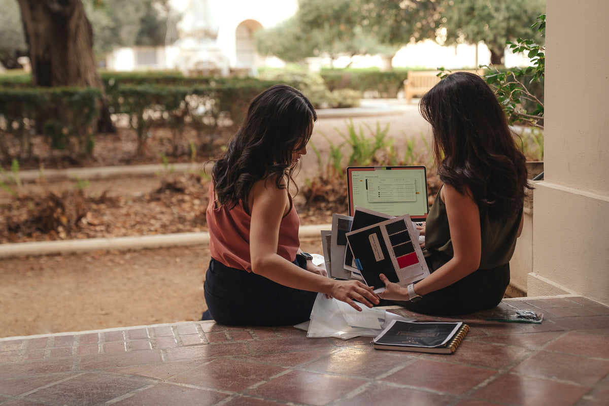 The Petite Standard founders choosing fabric swatches beside a laptop